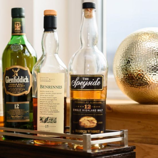 Vier Whiskyflaschen stehen auf einem Tablett. Rechts dahinter eine goldene Kugel auf der Holzfensterbank.