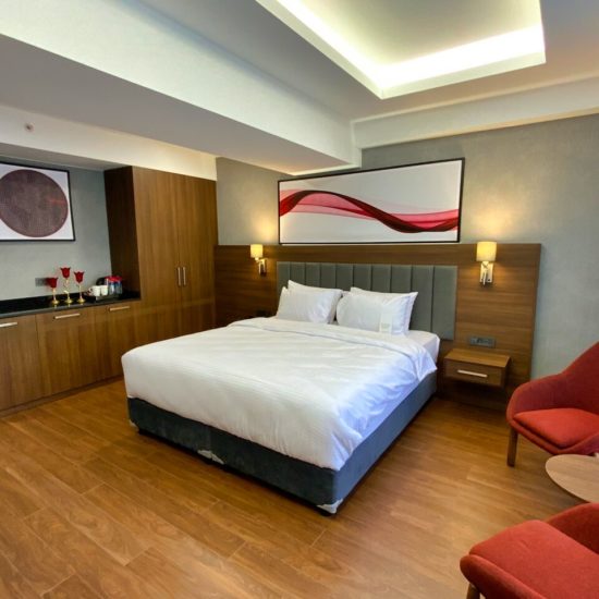 Doppelzimemr mit weiß bezogenem Bett, braunen Holzmöbeln und Holzboden sowie zwei roten Sesseln.