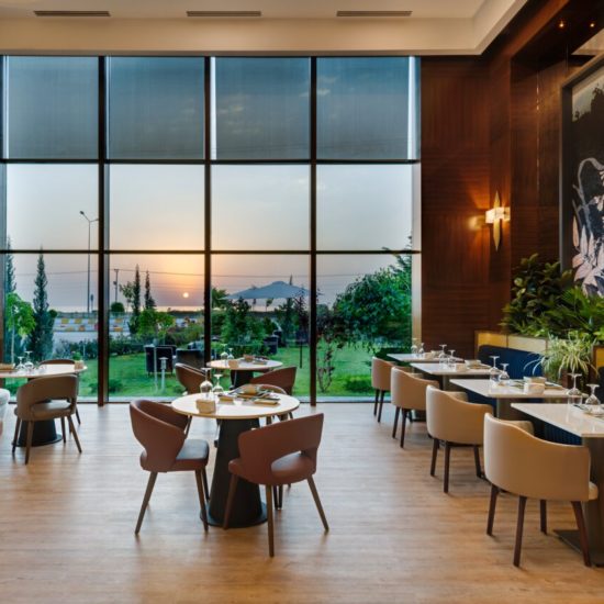 Hotelrestaurant mit großer Panoramascheibe und Sitzgruppen auf hellem Holzboden.