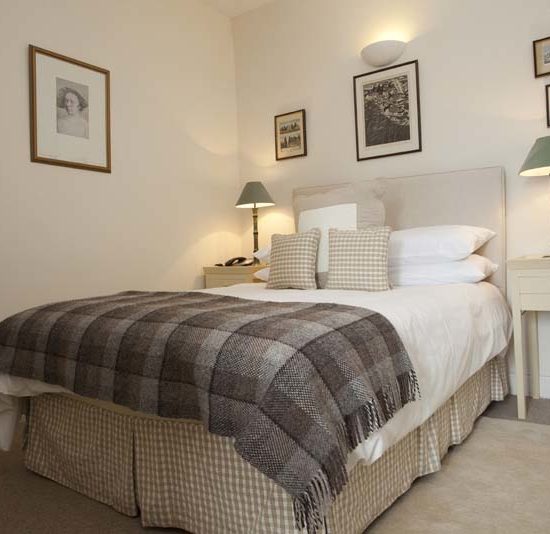 Hell gestaltetes Doppelzimmer mit brauem Bettüberwurf aus Tweed.