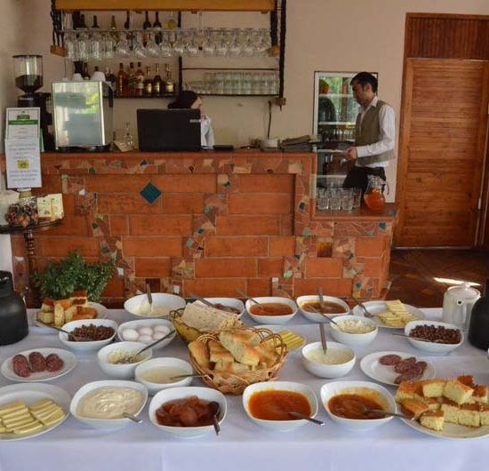 Frühstücksbuffet mit Brot und vielen Schalen mit Marmelade und Kompott. Im Hintergrund eine rotbraue Bar.