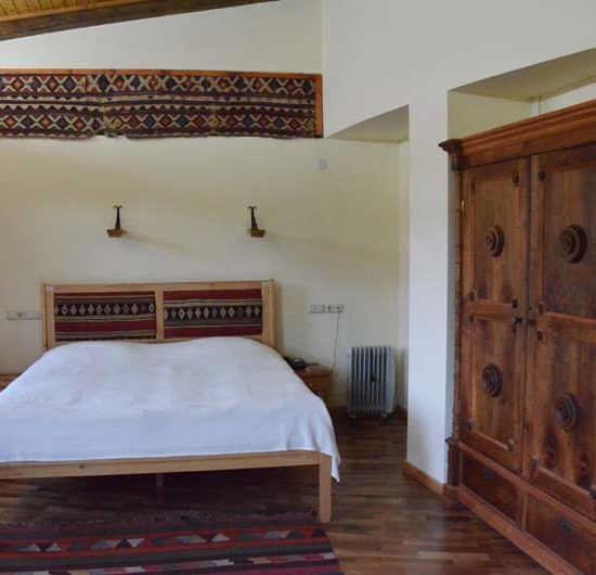 Doppelzimmer mit antikem Holzschrank, Holzboden und einem Kelim an der Wand. Das Bett mit weißer Decke.