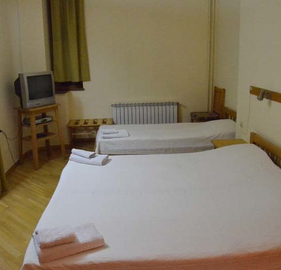 Einfaches Dreibettzimmer mit weißer Bettwäsche und schlichten Möbeln. Auf den Betten liegen Handtücher.