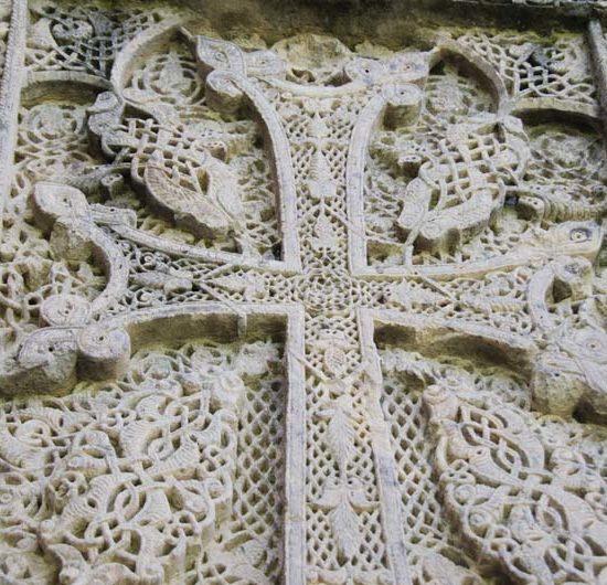 Filigranes Flächenrelief und ein in weißem Stein gehauenes Kreuz auf einem Kreuzstein in Goschawank in Armenien.