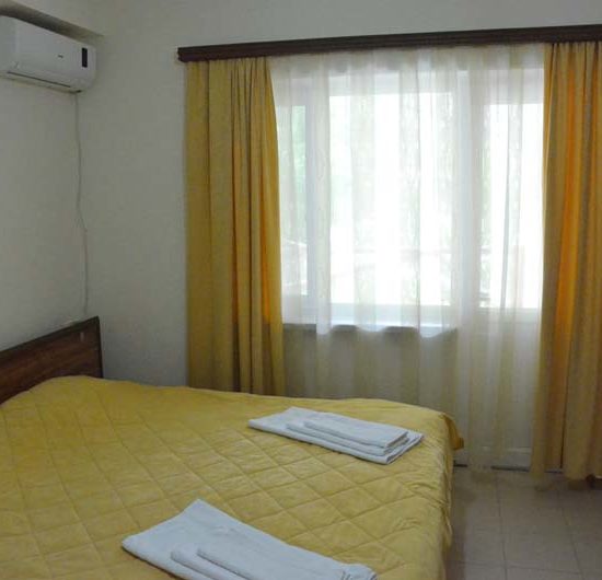 Doppelzimmer mit gelber Bettdecke, gelben Gardinen und weißen Wänden.