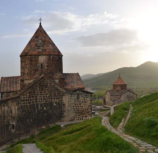 Gepflasterte Wege führen zu zwei steinernen Rundkuppelkirchen, die oberhalb des Sewan Sees in der Berglandschaft Armeniens liegen.