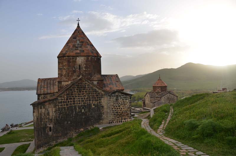 Gepflasterte Wege führen zu zwei steinernen Rundkuppelkirchen, die oberhalb des Sewan Sees in der Berglandschaft Armeniens liegen.