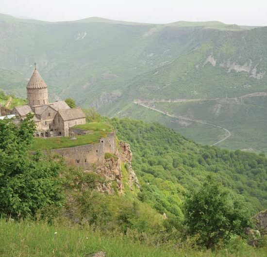 Die steinerne Klosteranlage Tatev mit rundem Kirchturm klebt wie ein Schwalbennest an den Hängen einer grün bewachsenene tiefen Schlucht.