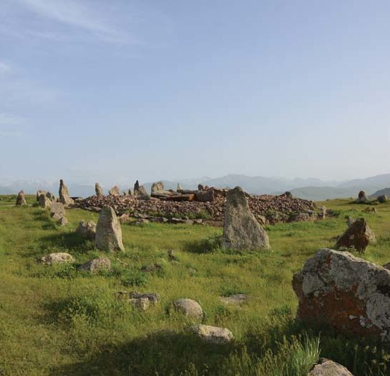 Prähistorischer Steinkreis Zorats Kar mit stehenden Steinen inmitten einer grünen Wiese. Im Hintergrund die Berge Armeniens