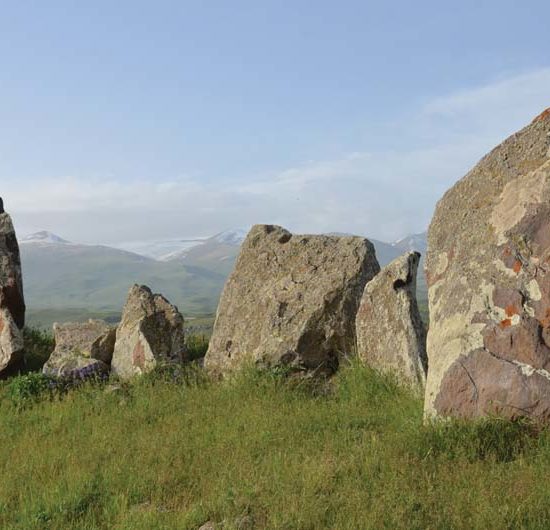 Eine Reihe stehender Basalt-Felsbrocken von Zorats Kar vor den schneebedeckten Bergen Armeniens.