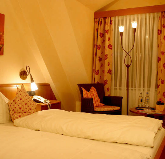 Doppelzimmer des Hotels Nassau-Oranien in hellen Gelb- und Rottönen.