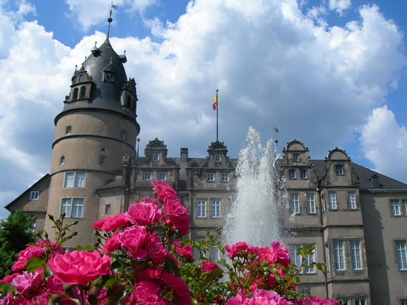 Renaissanceschloss Detmold mit Wehrturm und Elementen der Weserrenaissance. Im Vordergrund rosa Rosen und die Fontäne eines Springbrunnens.