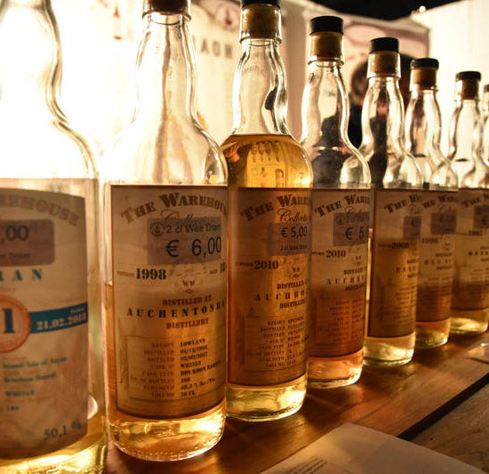 Eine lange Reihe von Whiskyflaschen vom Warehouse No. 8 leuchten vor hellem Hintergrund.