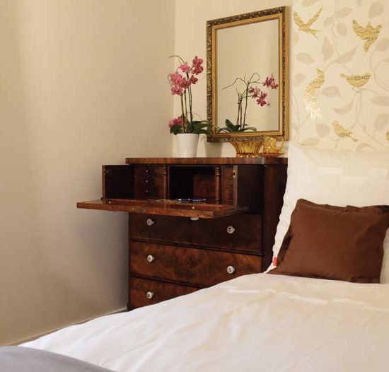 Bett vor einer Vogeltapete und neben einer antiken Schreibkommode, auf der eine Orchidee steht.