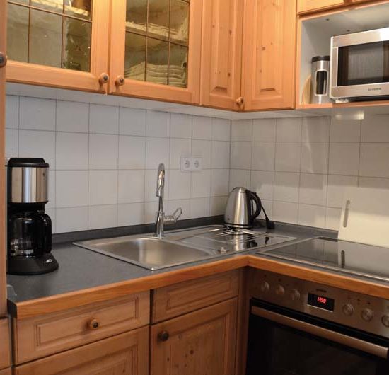 Ecke einer Küchenzeile mit mittelbraunen Echtholzfronten, Mikrowelle, Backofen, Spüle und Kaffeemaschine.