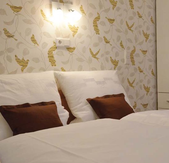 Doppelbett mit eleganter weißer Bettwäsche und braunen Dekokissen vor einer abstrakten Vogeltapete.