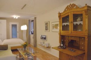 Wohn-Schlafraum mit antikem Buffetschrank in Fichtenholz, Glastisch, Sofa und Doppelbett.
