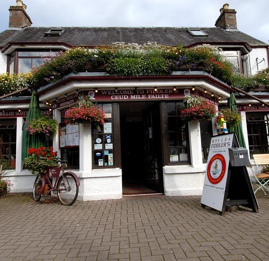 Blumengeschmückter schottischer Pub mit Sitzgarnituren vor dem Haus.