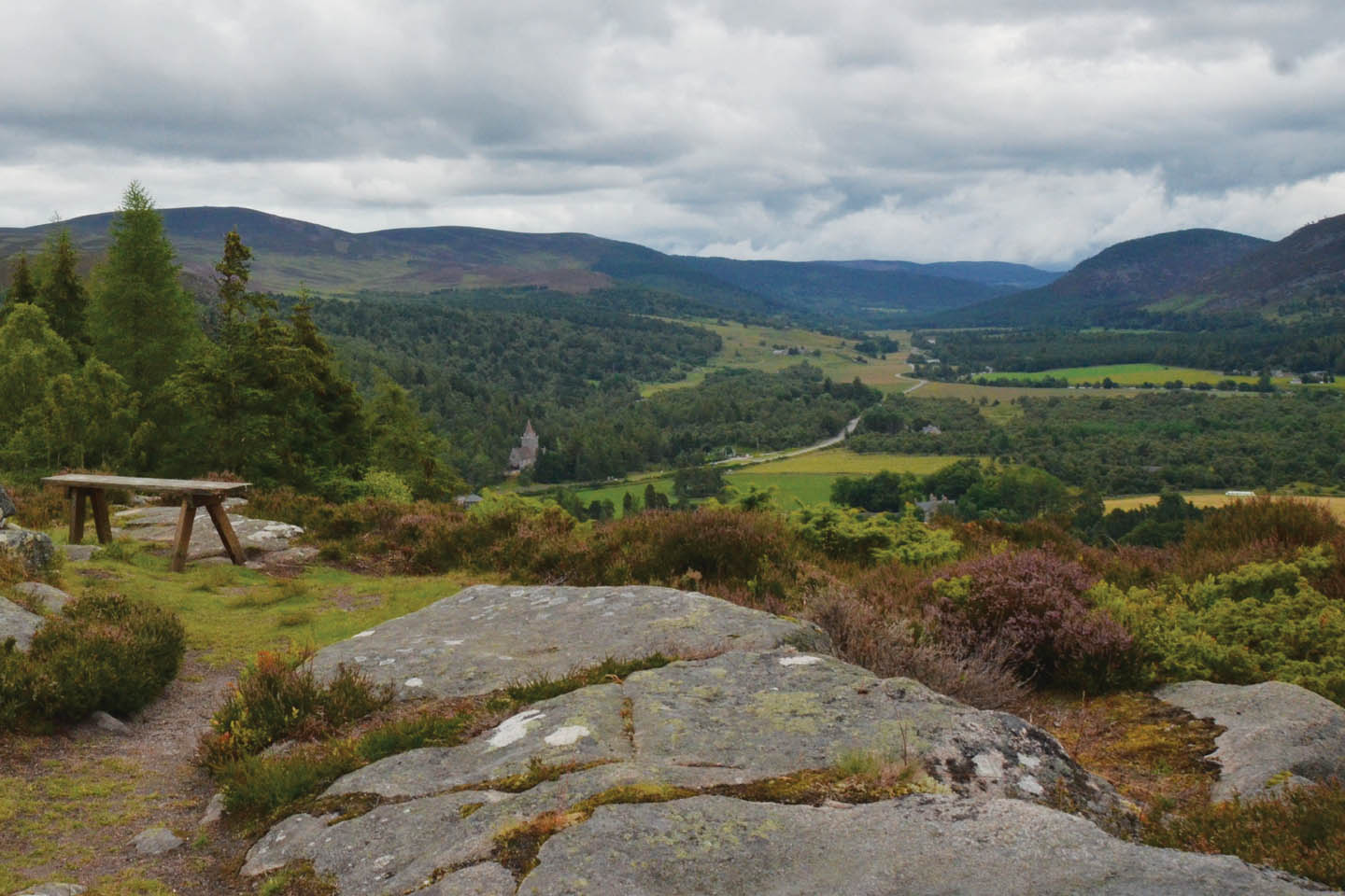 Blick von einem Steinplateau mit Heidekraut und Bank über ein Tal in den schottischen Highlands bei Balmoral.