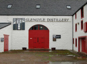 Weißes Gebäude der Glengyle Distillery mit großem roten Tor.