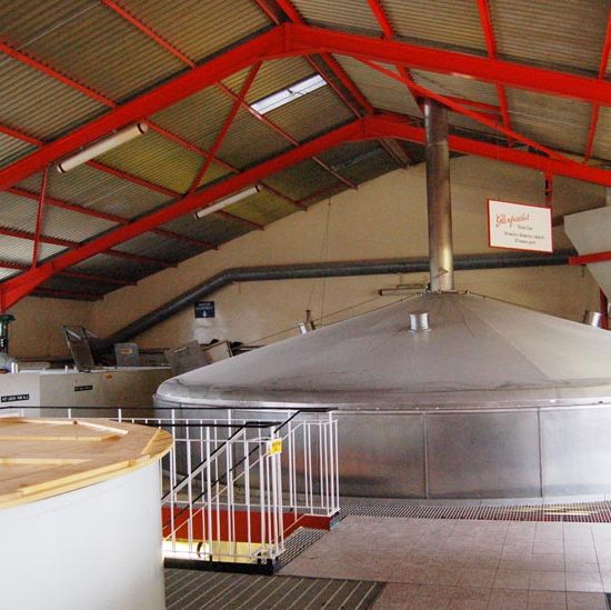 Edelstahl-Maischebottisch von Glenfarclas Distillery in einer Lagerhalle mit rot gestrichenen Dachträgern.