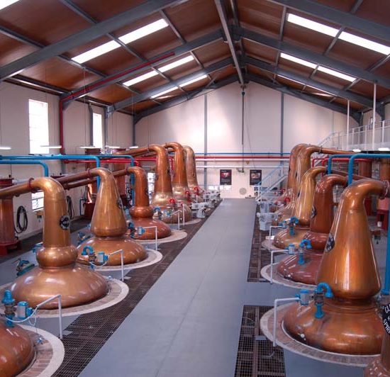 Blick von oben in das moderne Stillhouse der Glenfiddich Destillerie mit sechs bzw. sieben Kupferbrennblasen an jeder Seite des Mittelganges.