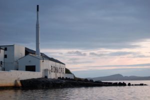 Weiß gestrichene Destillerie Bowmore im Abendlicht am Meer.