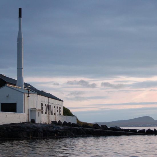 Weiß gestrichene Destillerie Bowmore im Abendlicht am Meer.