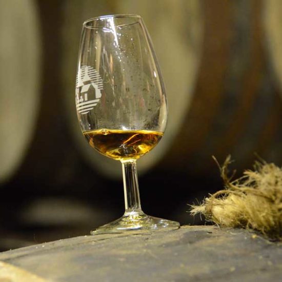 Großaufnahme von einem Whiskyglas mit Logo der Bowmore Distillery auf einem Whiskyfass.