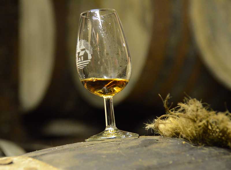Großaufnahme von einem Whiskyglas mit Logo der Bowmore Distillery auf einem Whiskyfass.