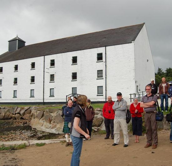 Reisegruppe hört dem Guide von Laphroaig zu, während sie vor der Destillerie stehen.