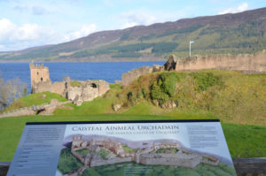 Schaubild einer schottischen Burganlage mit den Ruinen von Urquhart castle und dem See Loch Ness im Hintergrund.