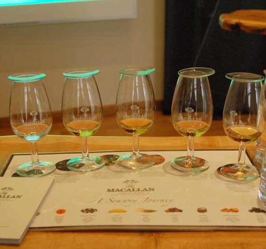Whisky Tasting-Map von Macallan, auf dem die Sensory Journey abgebildet ist. Darauf stehen mit Glassdeckeln abgedeckte Whisky Nosinggläser sowie Wassergläser.