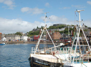 Schiffe im Hafenbecken der schottischen Stadt Oban, die von einem runden Fort überragt wird.