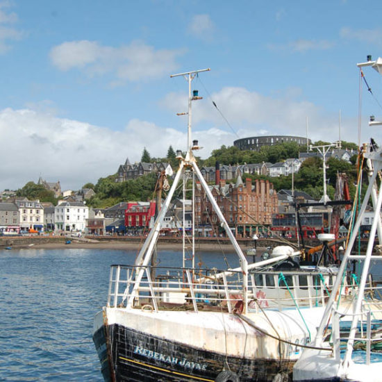 Schiffe im Hafenbecken der schottischen Stadt Oban, die von einem runden Fort überragt wird.