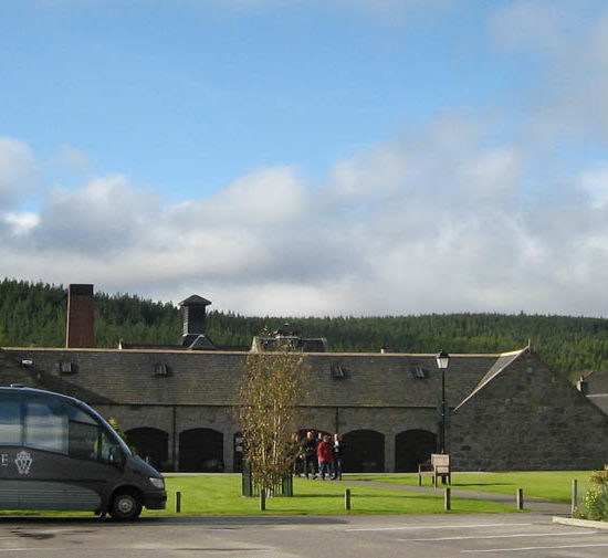 Schwarzer Minibus von Prestige parkt vor den niedrigen Steingebäuden der Royal Lochnagar Destillerie.