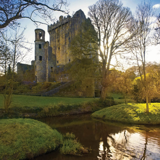 Sonnige Herbststimmung mit der Ruine des wehrhaften irischen Blarney Castle inmitten des Parks mit Bachlauf.