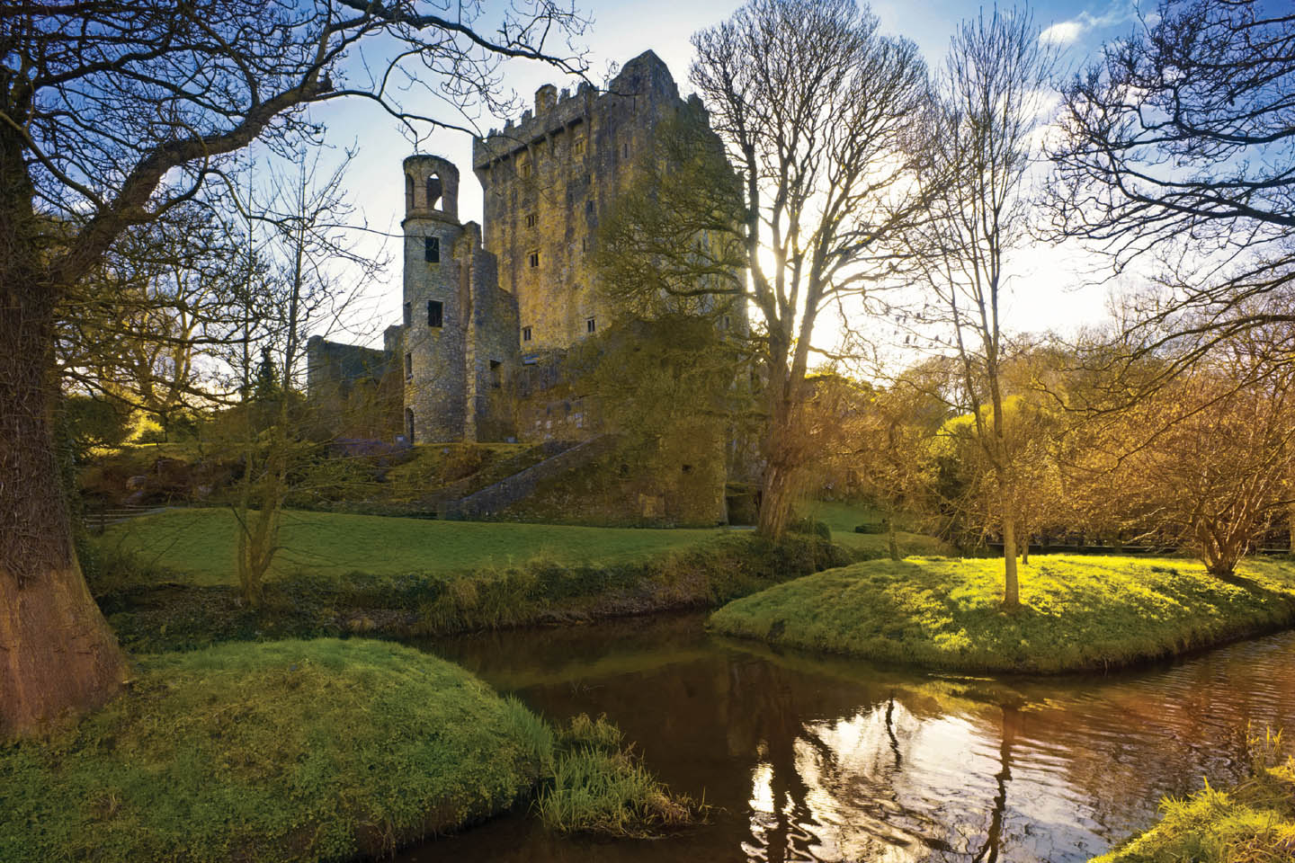 Sonnige Herbststimmung mit der Ruine des wehrhaften irischen Blarney Castle inmitten des Parks mit Bachlauf.