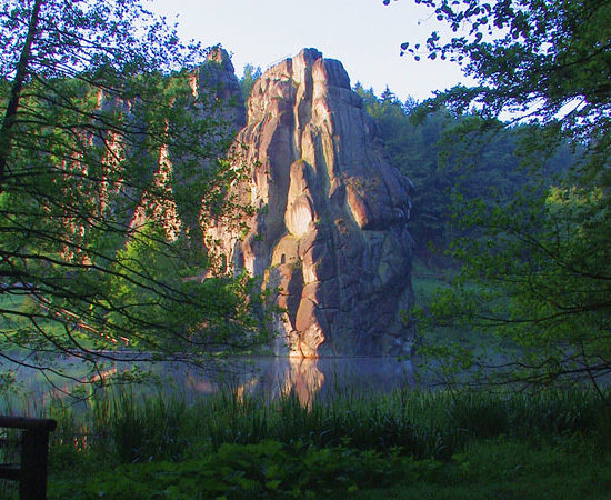 Die Felsgruppe der Externsteine wird bei Morgenstimmung gerahmt vom aufsteigenden Dunst des Teiches und Bäumen des Hudewaldes.