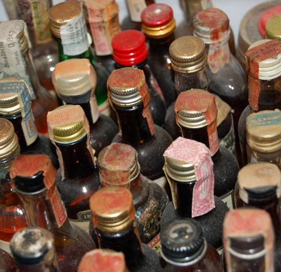 Eine Sammlung von alten, verstaubten Whiskysamples mit farbigen Verschlüssen und Banderolen.