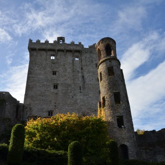 Eine wehrhafte Schlossruine mit rundem Turm ragt in einen blauen, leicht bewölkten Himmel.