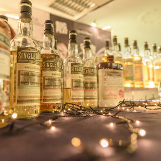 Eine Reihe fast gleicher Single Malt Whiskyfalschen steht beim Bottle Market Bremen auf einem Tisch mit Lichterkette und einem Glaskrug mit Wasser.