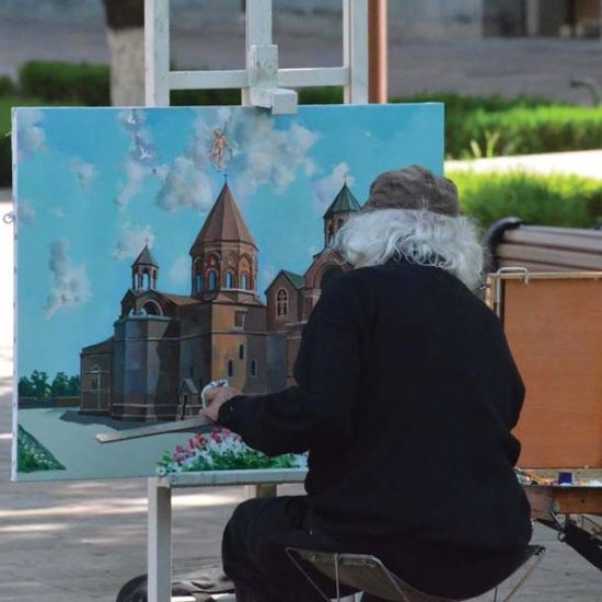 Maler in schwarzer Kleidung und mit langem weißen Haar sitzt vor einer Staffelei und malt die Kathedrale von Etschmiatsin in Armenien.