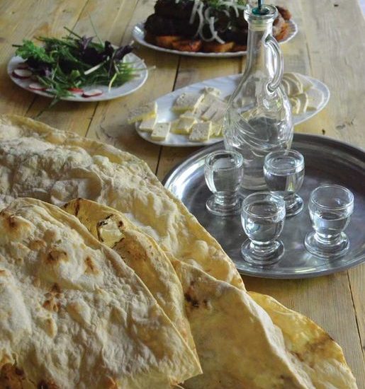 Das armenische Brot Lavash liegt auf einem Holztisch. Daneben ein silbernes Tablett mit Schnapsgläsern und Karaffe sowie Käse und Kräuter.