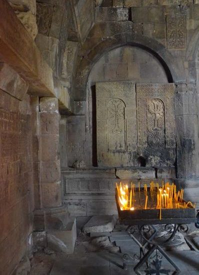 Innenraum der Klosterkirche Norawank mit zwei filigran reliefierten Kreuzsteinen und gelben Kerzen auf einem eisernen Tablett.