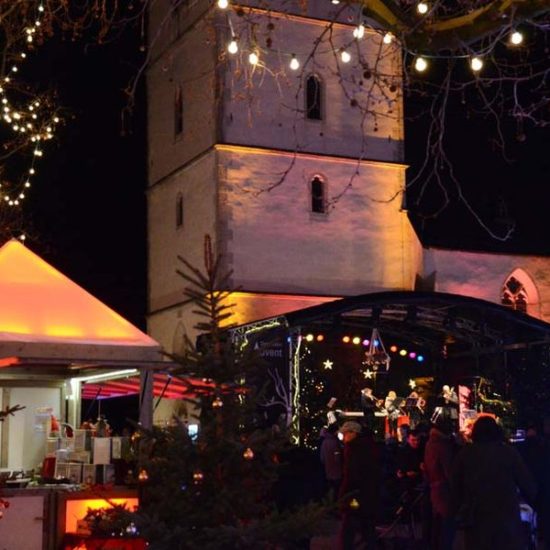 Bühne und beleuchteter Stand auf dem Weihnachtsmarkt Detmold. Im Hintergrund der weiße Turm der Erlöserkirche am Markt.