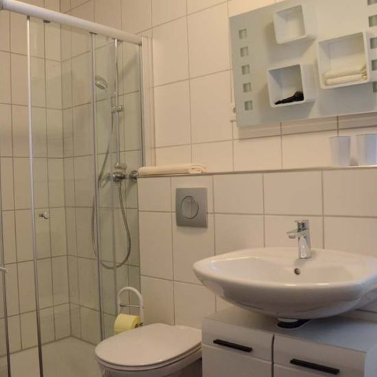 Hell gefliestes Badezimmer mit Dusche, Toilette und Waschbecken.