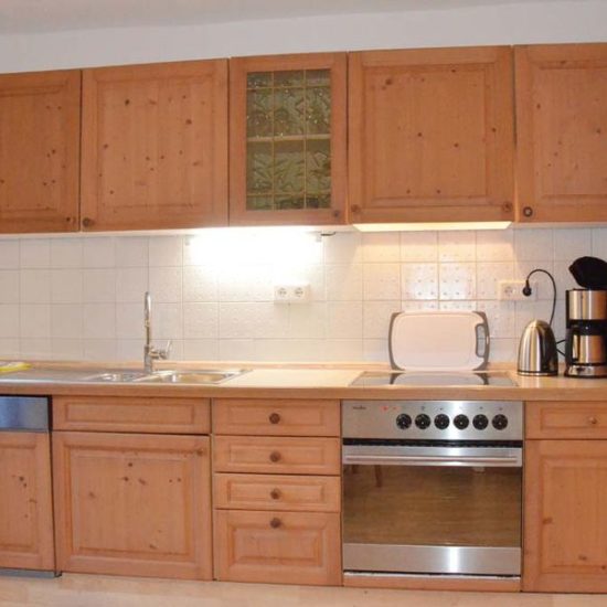 Küchenzeile mit Fichten-Echtholzfront, Spülmaschine, Backofen, Wasserkocher und Kaffeemaschine.