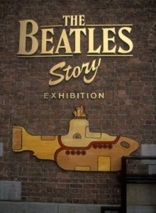 Dunkelrote Backsteinwand mit goldenem Werbeschriftzug The Beatles Story Exhibition und darunter einem gelb-goldenen U-Boot.