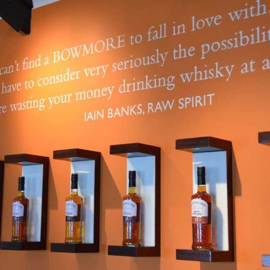 Orangene Wand mit Zitat von Iain Banks und einer Reihe von Whiskyflaschen von Bowmore.